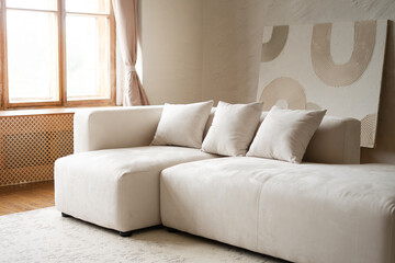 White modern beige sectional sofa with cushions and abstract art on wall. Contemporary minimalist interior design for living room or studio.