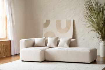 A spacious living area showcases a contemporary sectional sofa adorned with cushions, complemented by a large dried palm plant in a bright and airy setting.
