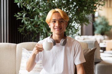 Asian teenager man with blonde hair inside cafe restaurant holding coffee cup