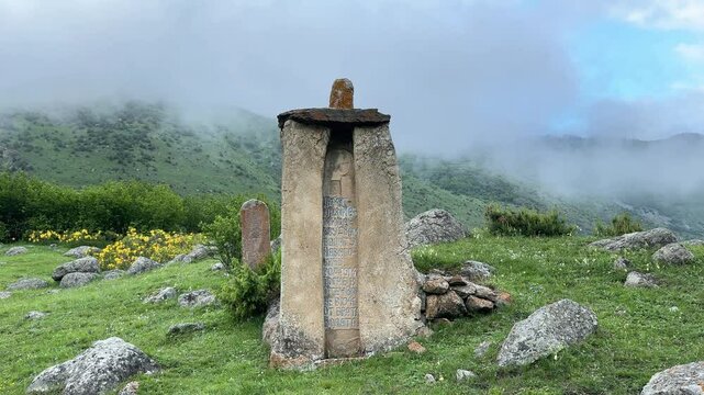 Ancient old Ossetian burial burials, vertical stone monument. Slab with ornaments on a mountain slope in a cloudy haze in North Osetia, Russia
