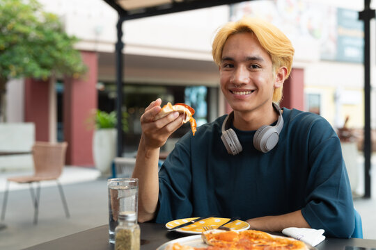 Thai gay teen male eating pepperoni pizza in outdoor restaurant - Powered by Adobe
