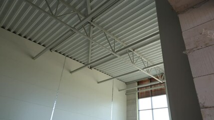 A view of a modern industrial interior with a high metal ceiling, steel trusses, corrugated panels, and unfinished concrete walls illuminated by daylight through large windows - Powered by Adobe