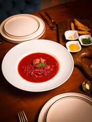 Traditional Ukrainian borscht with beef and dill served in a white bowl, styled with condiments and pastry on a warm wooden restaurant table.