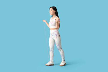 Sporty young Asian woman with skipping rope on blue background