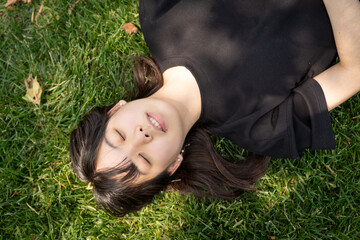 A teenage girl lies on the grass with her eyes closed, enjoying a quiet moment under the sun, appearing calm and relaxed.