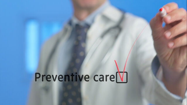 Doctor wearing a lab coat and stethoscope, checking a box next to the words preventive care displayed on a virtual screen, emphasizes the importance of proactive health management