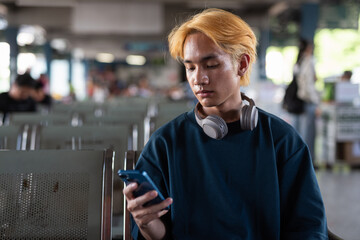 Young Asian tourist man in bus station texting with phone