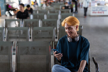 Young Asian tourist man in bus station texting with phone