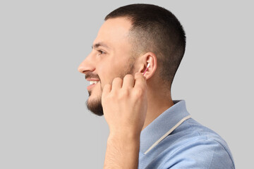 Fototapeta premium Young man cleaning ears with cotton buds on grey background