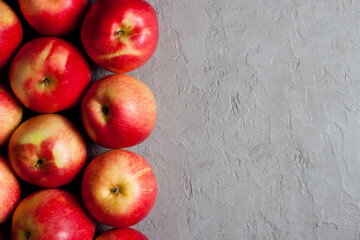 A row of vibrant red apples lines the left side of a textured light gray plaster background. Minimalist design. Copy space