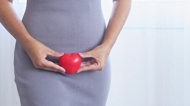 Close-up of a woman holding a red heart-shaped object, representing vaginal discharge, menopause, reproductive system care, and gynecological health awareness - Powered by Adobe