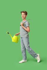 Teenage boy with watering can and rake on green background