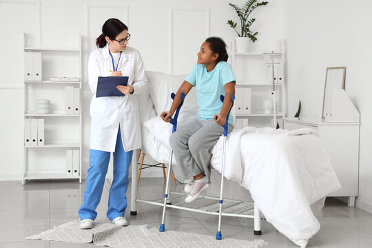 Teenage African-American girl with crutches and doctor in hospital room - Powered by Adobe