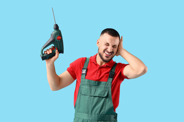 Male worker with drill suffering from loud noise on blue background