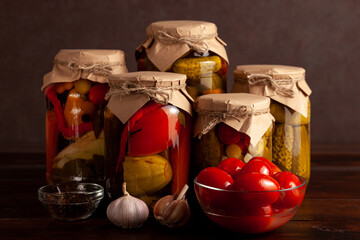 Jars of assorted homemade pickled vegetables, tomatoes, garlic, and spices on a rustic wooden table. Perfect for harvest, organic food, or kitchen-themed projects.