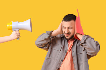 Young man with foam hand and megaphone suffering from loud noise on yellow background