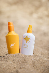 Sunscreen bottles with SPF  placed on sandy beach, emphasizing skincare during sunny summer....