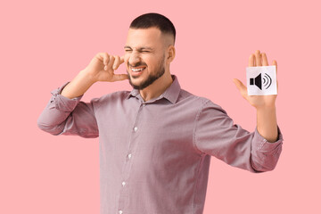 Young man with speaker icon suffering from loud noise on pink background