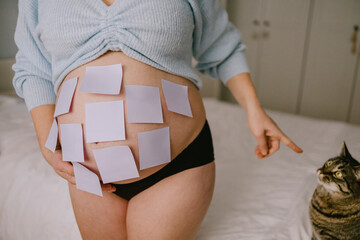 Pregnant Woman with Sticky Notes on Belly, Expecting Baby, Creative Maternity Concept with Cat in Background