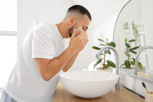 Young man washing his face with soap near sink in bathroom - Powered by Adobe