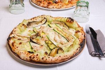 Pizza tradizionale napoletana con crema di zucchine, zucchine grigliate, petto di pollo piastrato e mozzarella servita in una pizzeria 