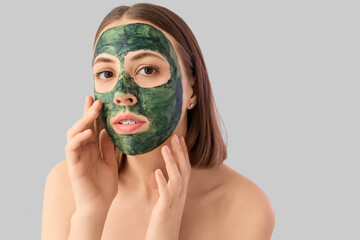 Young woman with spirulina facial mask on light background, closeup