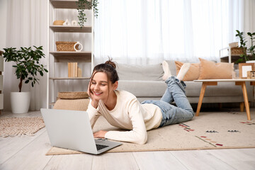 Beautiful young woman with laptop resting on floor at home