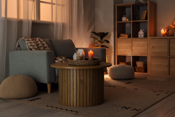 Interior of living room with sofa and burning candles on table at night