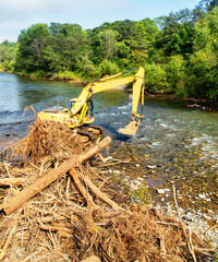 Universal excavator capabilities. An excavator removes trees from the riverbank, where they got...