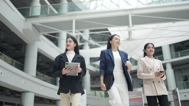 Three women are walking in a building. One of them is holding a tablet. The other two women are holding cell phones