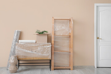 Wrapped furniture and things with stretch film near beige wall in room on moving day