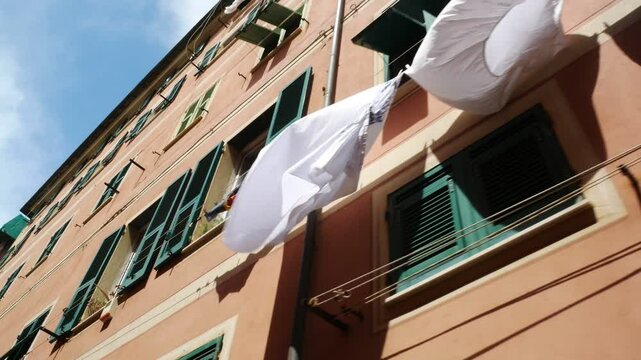 Bed sheets and various clothes hanging for drying outside of a colorful traditional building in the historical centre of Nervi, Genoa, Italy.