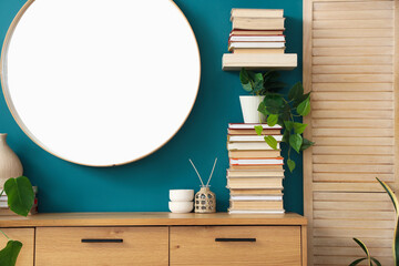 Chest of drawers with books and mirror on blue wall in room. Closeup