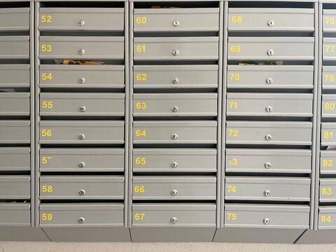  A full-frame close-up of numerous light grey metal mailboxes with yellow numbers and small keyholes, - Powered by Adobe