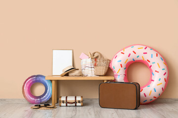 Suitcases with inflatable rings, summer bag and beach accessories on bench near beige wall. Vacation concept