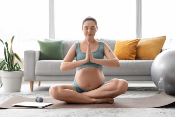 Sporty pregnant woman meditating on mat at home
