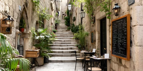 Photo sur Plexiglas Charming narrow stone alley with stairs, outdoor cafe tables, greenery and a handwritten menu board