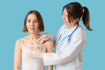 Female doctor applying mustard plaster on patient's chest against blue background