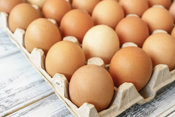 Brown chicken eggs in a cardboard tray on a rustic wood background for farm and food concepts and healthy eating or cooking recipes and ingredients advertising.