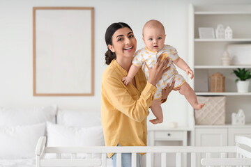 Beautiful young happy mother with her cute little daughter near crib at home