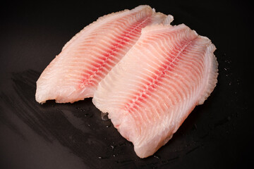 Fresh tilapia fillet on black background, top view.