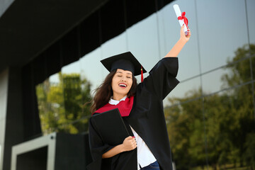 Female Asian graduating student with diploma and book near university