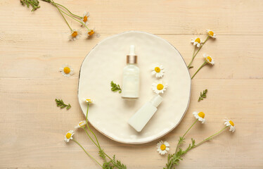 Composition with plate, chamomile flowers and bottles of cosmetic products on wooden background