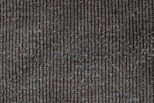 Macro texture of gray fabric with lots of pilling and damage on the surface.