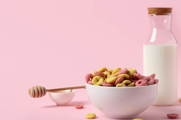 Bowl with tasty cereal rings and bottle of milk on pink background