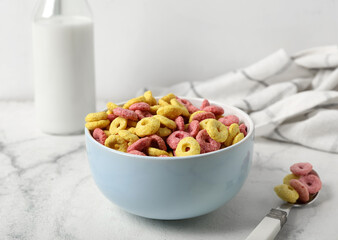 Bowl with tasty cereal rings, spoon and bottle of milk on light background