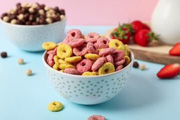 Bowls of tasty cereal rings and chocolate corn balls with strawberries on color background