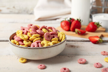 Bowl with tasty cereal rings and strawberries on light wooden background