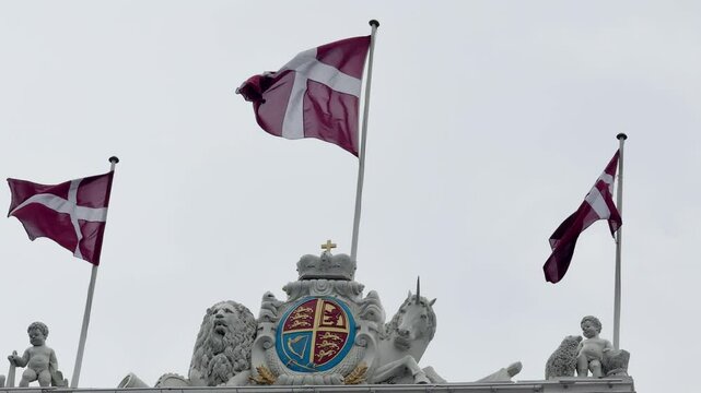 Three flags of Denmark waving in the wind with a background of grey moody sky