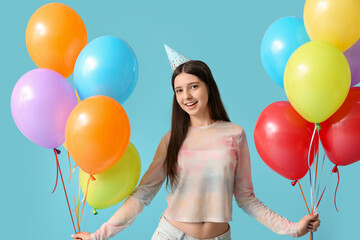 Beautiful teenage girl in party hat with colorful air balloons on blue background